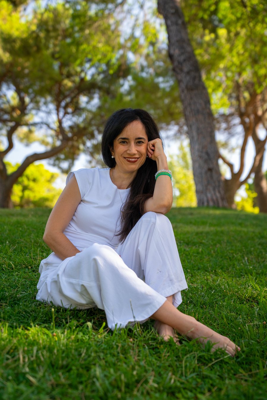 Diana Texeira sentada en la hierba de un parque, sonriendo, vestida de blanco